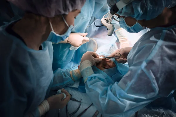 Ärzteteam im Operationssaal, dunkler Hintergrund. Im Operationssaal führt ein internationales Team professioneller Ärzte in einem modernen Operationssaal eine Operation durch. Sparen — Stockfoto