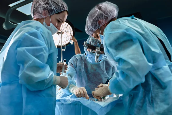 Chirurgický tým na operačním sále, zblízka. Mezinárodní tým profesionálních lékařů na moderním operačním sále podstupuje chirurgický zákrok. Zachraňování životů, moderní medicína, modré světlo — Stock fotografie