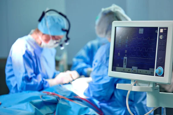 Электрокардиограмма в стационарной хирургии операционная скорой помощи показывает частоту сердечных сокращений пациентов с размытым составом хирургов — стоковое фото