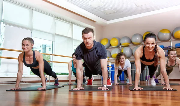 A group of sporting young people in sportswear, in a fitness room, doing push-ups or planks in the gym. Group fitness concept, group workouts, motivation — Stock Photo, Image