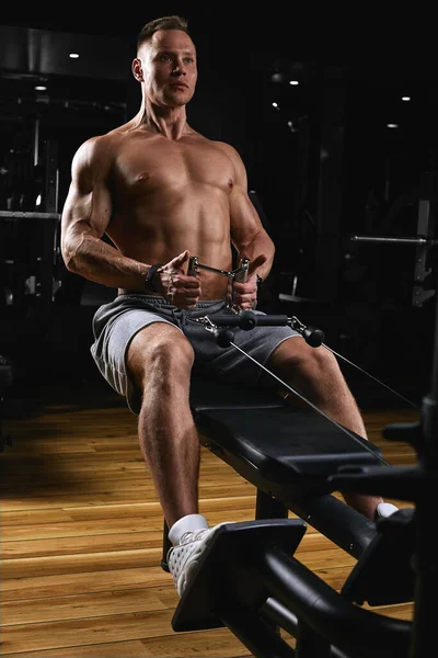 Atletik vücutlu, karanlık bir spor salonunda spor aletleri üzerinde egzersiz yapan güçlü bir gencin yan görüntüsü. Kopyalama alanı, reklam afişi, fitness motivasyonu, sağlıklı beden sağlığı — Stok fotoğraf