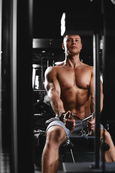 一个身强体壮的年轻人在一间黑暗的健身房里用健身器材做运动的侧视图。复制空间，广告横幅，健身动机，健康的身体健康的头脑 — 图库照片