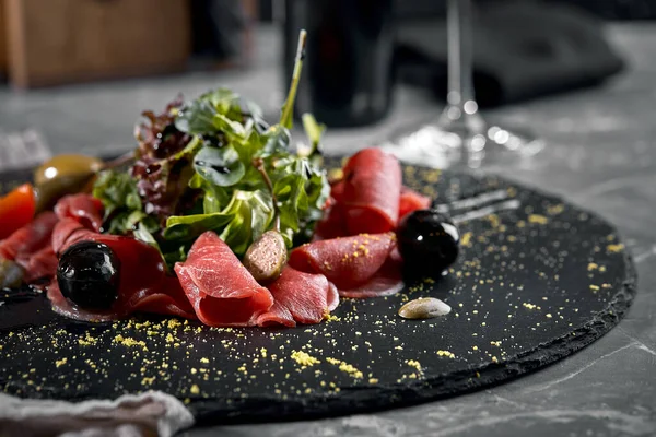 Rundvleescarpaccio met arugula op een zwart bord, traditionele Italiaanse keuken. Donkere sleutel, kopieer ruimte, — Stockfoto