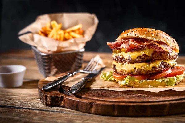 Šťavnatý burger na desce, černé pozadí. Tmavé pozadí, fast food. Tradiční americké jídlo. Kopírovat prostor. — Stock fotografie