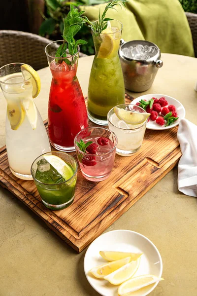 Letnie napoje bezalkoholowe, zestaw lemoniad. Lemoniady w dzbankach na stole, których składniki są wykonane są rozmieszczone wokół. — Zdjęcie stockowe