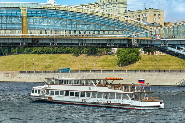 Moscú, Rusia - 29 de mayo de 2019: Moderno barco fluvial en el fondo del puente en la ciudad. El barco navega en el río de la ciudad navegando bajo los hermosos puentes de la ciudad en el río — Foto de Stock