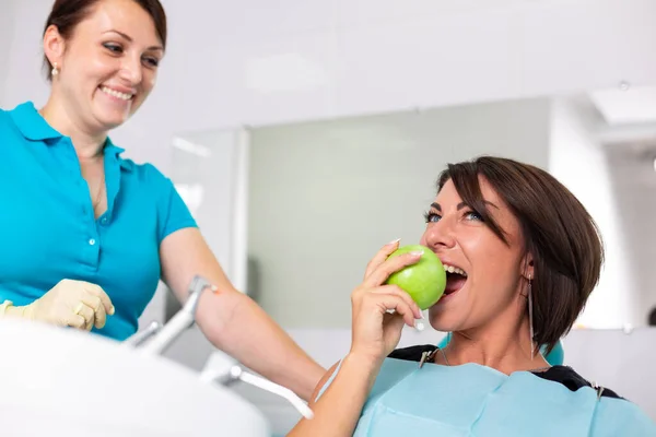 Szczęśliwy pacjent na przyjęciu u stamatologa, sprawdza stan zębów, gryzie zielone jabłka. Koncepcja stomatologii, zdrowe zęby, piękny uśmiech. — Zdjęcie stockowe