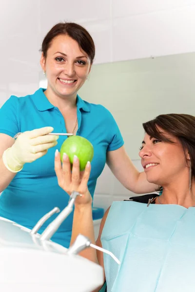 Счастливый пациент на ресепшене у статолога, проверяет здоровье зубов, кусает зеленые яблоки. Концепция стоматологии, здоровые зубы, красивая улыбка . — стоковое фото