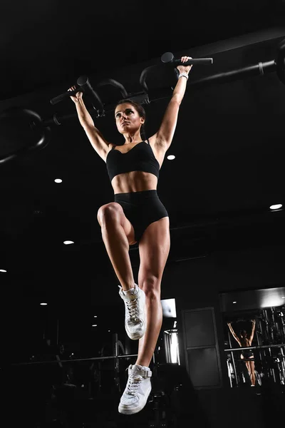 Frau beim Training im Fitnessstudio - Klimmzüge. Bild kreuzbearbeitet, kontrastreiches, dunkel körniges Bild. — Stockfoto