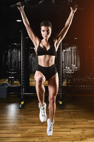 Frau beim Training im Fitnessstudio - Klimmzüge. Bild kreuzbearbeitet, kontrastreiches, dunkel körniges Bild. — Stockfoto