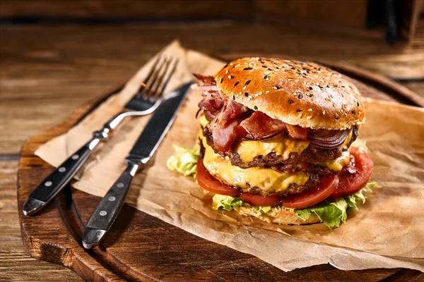 Šťavnatý americký burger, hamburger nebo cheeseburger se dvěma hovězími placičkami, s omáčkou a opečeným černým pozadím. Koncept amerického rychlého občerstvení. Kopírovat prostor — Stock fotografie