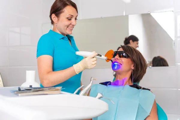 O dentista brilha nos dentes dos pacientes com uma lâmpada ultravioleta para fixar o selo dental . — Fotografia de Stock