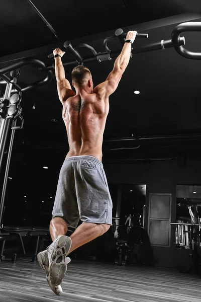 Ισχυρός άνδρας κάνει pull-ups σε μια γραμμή σε ένα γυμναστήριο. — Φωτογραφία Αρχείου
