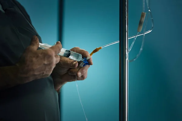 Doctors hand and infusion are dripping in the hospital on a blurred background. Blue background, low key, dramatic picture, saving lives. — Stock Photo, Image