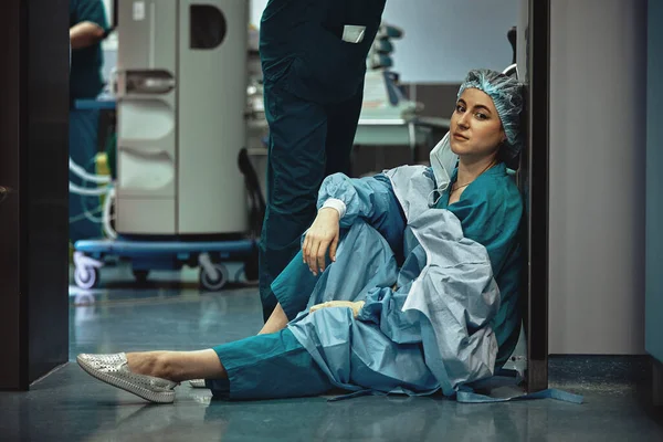 Médico cansado sentado após a cirurgia no corredor do hospital. Grande fardo para os médicos e para a medicina. Descansa depois do trabalho. Epidemia, falta de pessoal médico, enfermarias médicas . — Fotografia de Stock