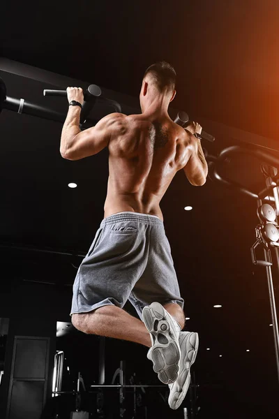 Ο αθλητής κάνει pull-ups - πηγούνι στο γυμναστήριο, μοντέλο με ένα αθλητικό σώμα τόπλες. Πυροβολήθηκε από πίσω, με χαμηλό κλειδί., — Φωτογραφία Αρχείου