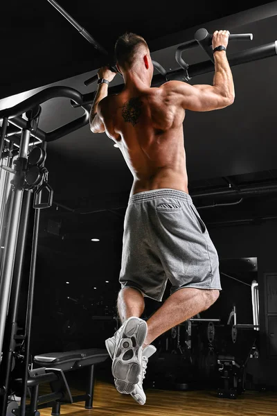Der Sportler macht Klimmzüge - Kinn im Fitnessstudio, Modell mit einem Sportkörper oben ohne. Schuss von hinten, leise, — Stockfoto