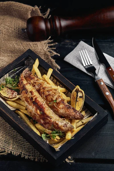 Concepto de pescado y patatas fritas, comida tradicional inglesa, pescado frito y papas fritas. Fondo oscuro, estilo rústico, fondo de madera, espacio para copiar. Vista desde arriba — Foto de Stock