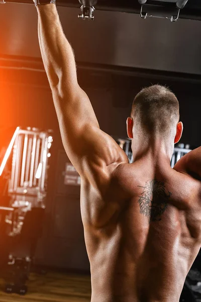 El atleta hace un pull-up en la barra horizontal. Un hombre en gran forma está haciendo pull-ups en la barra horizontal desde el hall de entrada. Fondo oscuro, motivación deportiva . — Foto de Stock