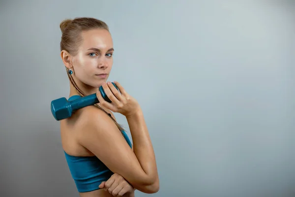 Beautiful fitness model doing exercises with dumbbells in hands on a gray background. Close-up. Woman posing on camera with dumbbells. Healthy lifestyle. Achieving goals, sports motivation. Copy space