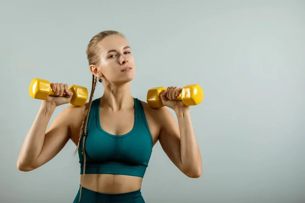 Спортивная женщина с гантелями в руках на сером фоне, фитнес-баннер, фитнес-мотивация. Фото мышечной фитнес-модели, работающей с гантелями на сером фоне . — стоковое фото