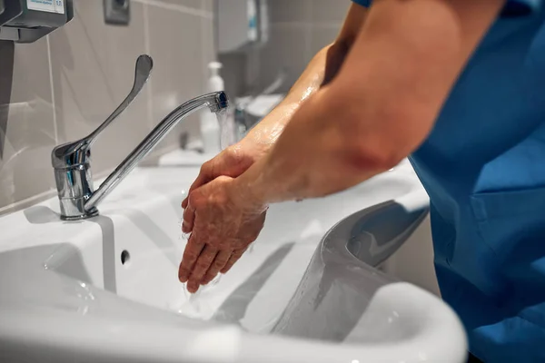 Close-up of a doctor washing his hands using a disinfectant dispenser.