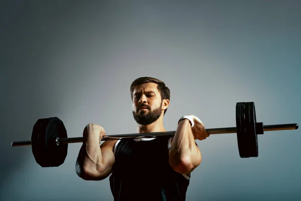 Un hombre hace ejercicios con una barra sobre un fondo gris. Concepto de fitness, motivación deportiva . —  Fotos de Stock