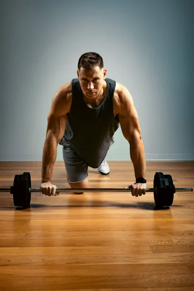 Un hombre hace ejercicios con una barra sobre un fondo gris. Concepto de fitness, motivación deportiva . —  Fotos de Stock