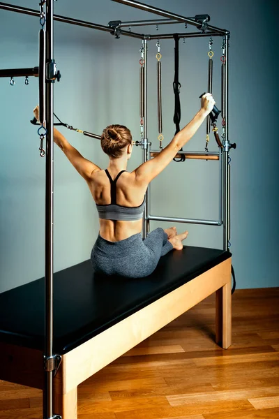 Young girl exercises on a bed of Pilates reformers, in the hall on a background of a gray wall. Fitness stretching concept. Healthy body, yoga, Pilates, copy space — Stock Photo, Image