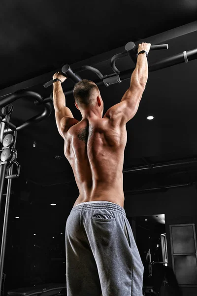 Mężczyzna podciąga się na poziomej sali gimnastycznej, ciemne tło, piękne ciało, motywacja fitness. — Zdjęcie stockowe