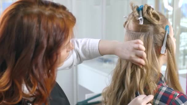 Um cabeleireiro profissional faz cachos com um ferro de cabelo. Cliente e cabeleireiro em um salão de beleza, indústria de beleza. Cuidados com o cabelo . — Vídeo de Stock