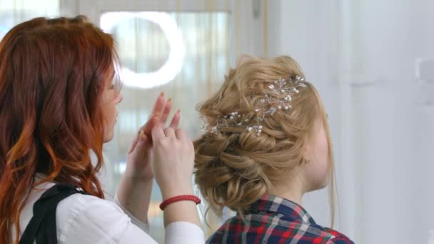 Fixando o cabelo com tiaras, um mestre de maquiagem anexa um carão de ramos ao penteado. Indústria da beleza, cuidados com o cabelo, preparação para a celebração . — Vídeo de Stock