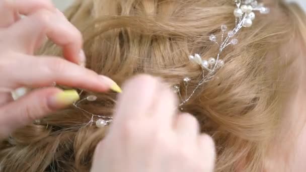 Um die Haare mit Tiaras zu fixieren, befestigt ein Make-up-Meister ein Ästchen an der Frisur. Schönheitsindustrie, Haarpflege, Vorbereitung auf das Fest. — Stockvideo