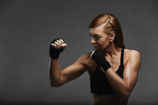 Boxer feminino com as mãos em bandagens boxer preto em uma postura boxer sobre um fundo cinza escuro, posando com uma chamada para a proteção. Objetivo realização, boxe, banner spot, espaço de cópia — Fotografia de Stock