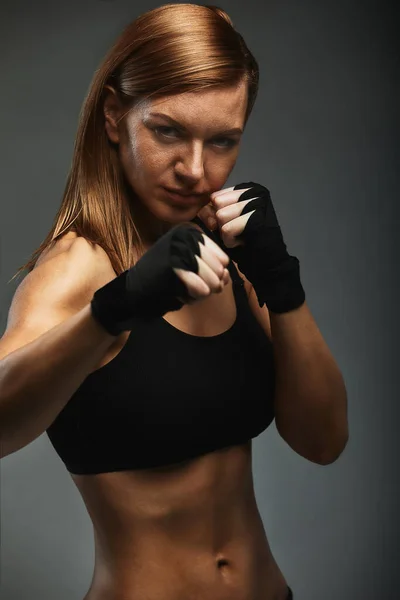 Boxeadora femenina con las manos en vendas de boxeador negro en una postura de boxeador sobre un fondo gris oscuro, posando con un llamado a la protección. Logro objetivo, boxeo, spot banner, espacio de copia — Foto de Stock