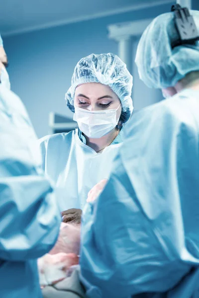 Kvinnlig kirurg med operationsassistenter. Kirurger under arbetet. Blå filter. Modern medicin med professionella läkare. — Stockfoto