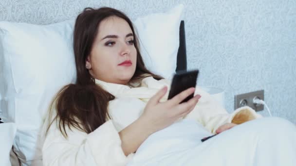 Ένα κορίτσι να μιλάει στο τηλέφωνο ενώ είναι ξαπλωμένη σε ένα rovat. Μοιραστείτε ειδήσεις κατά τη διάρκεια της καραντίνας, μείνετε σπίτι. Μοντέλο συν μέγεθος. Κοντινό πλάνο πορτρέτο μιας νοικοκυράς — Αρχείο Βίντεο