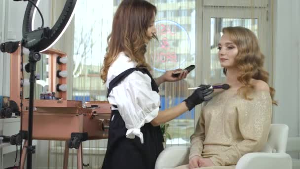 Professional make-up artist makes a make-up, make-up to a client in a beauty salon. Woman client in a beauty salon does makeup. The right image, the finishing touches, the beauty industry. — Stock Video