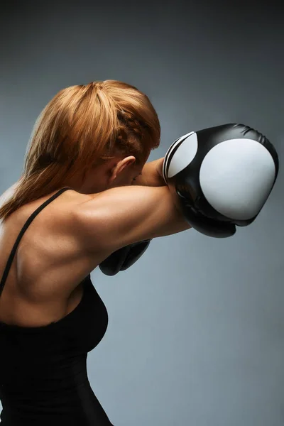 Hermosa mujer con guantes de boxeo negro sobre un fondo gris. Copiar espacio, banner deportivo, trabajo duro en sí mismo y su cuerpo . — Foto de Stock