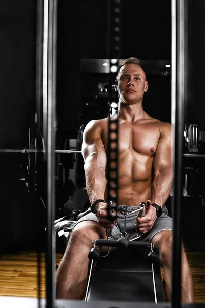 Zbliżenie na mężczyznę z nagim tułowiem ćwiczącego mięśnie pleców na symulatorze w hali sportowej. Zdjęcie z przodu. — Zdjęcie stockowe