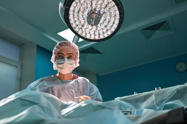 Close up portrait of young female surgeon doctor wearing protective mask and hat during the operation. Healthcare, medical education, surgery concept