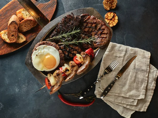 Surtido de carne a la parrilla, verduras y especias, una mesa de cocina para servir carne, con servilletas extendidas y cuchillos . — Foto de Stock