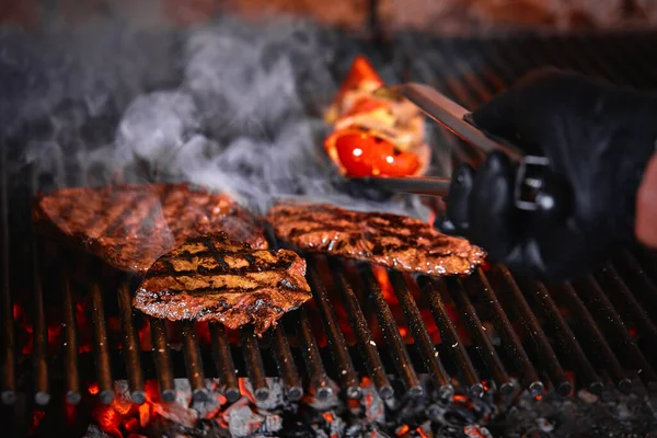 Čerstvé šťavnaté grilované maso s ohněm. Grilovací koncept, pečení masa na skutečném ohni s grilem a žhavým uhlím. — Stock fotografie