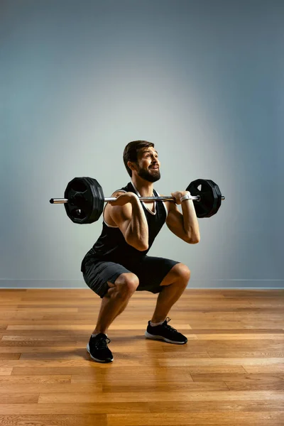 Un hombre hace ejercicios con una barra sobre un fondo gris. El cuerpo atlético de un joven en tensión muscular hace un acercamiento con una barra. Copiar espacio —  Fotos de Stock