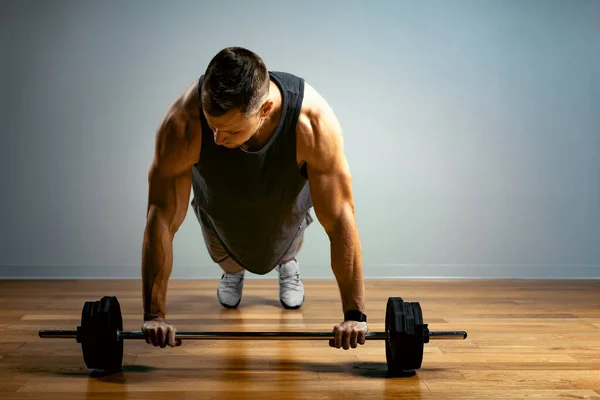 Un hombre hace ejercicios con una barra sobre un fondo gris. El cuerpo atlético de un joven en tensión muscular hace un acercamiento con una barra. Copiar espacio —  Fotos de Stock