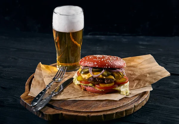 Lahodný burger s pivem a hranolky na dřevěném venkovském stole. Gamberger se salomovou cibulí a sekanou s půllitrem pěnového piva, tradiční americké jídlo. — Stock fotografie