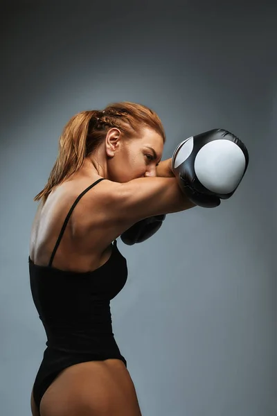 Sexy girl boxer com atlético bela figura em maiô preto e luvas de boxe em um fundo cinza. desafiar a si mesmo — Fotografia de Stock