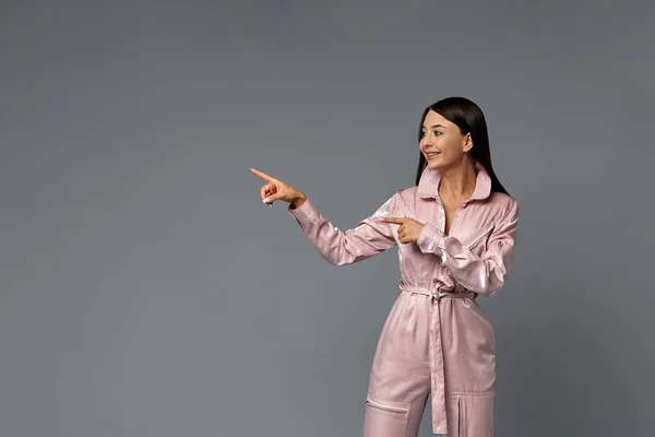 Modemädchen auf grauem Hintergrund zeigt auf Kopierfläche. Grauer Hintergrund, Mode, Kopierraum. — Stockfoto
