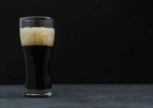 A pint of dark beer with foam, Dark background.