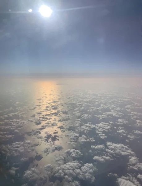 Sky travel. View from the illuminator. Fluffy white clouds. Sunlight pink and yellow reflexion on the water. Blue sky background. — Stock Photo, Image